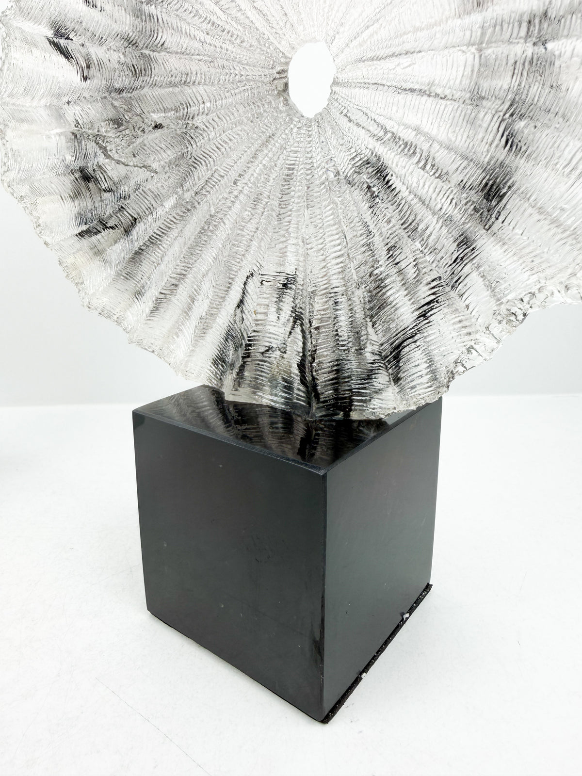 Sculpture décorative plissée en résine sur un socle en cristal noir élégant.