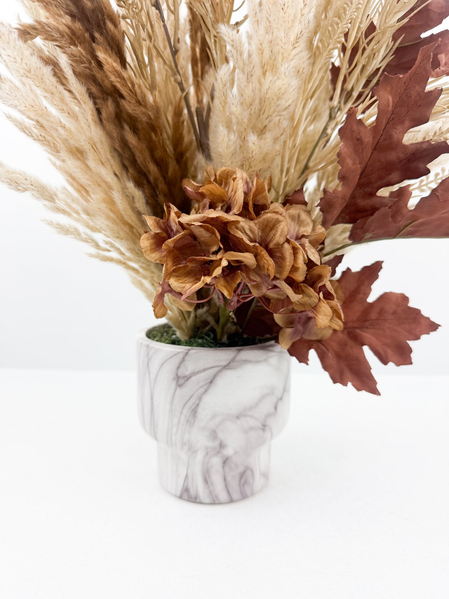 Fleurs séchées aux teintes chaudes et naturelles, présenté dans un élégant vase marbré.
