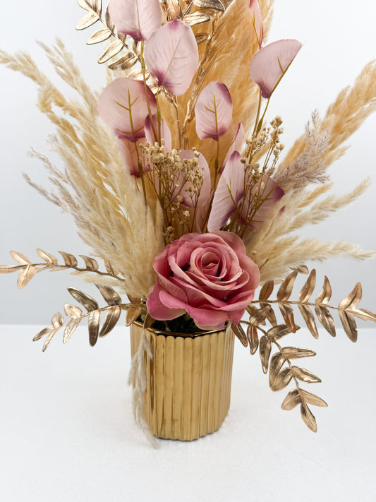 Fleurs séchées marron rehaussée d'une fleur rose délicate dans un vase en céramique doré au design élégant et luxueux.