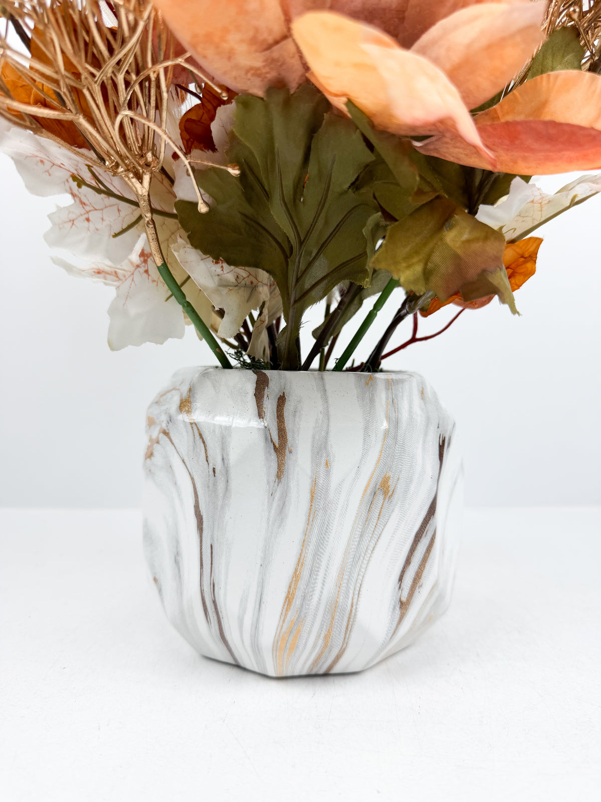 Magnifique fleurs aux nuances chaleureuses d'orange cuivré dans un élégant vase en céramique à effet marbré.
