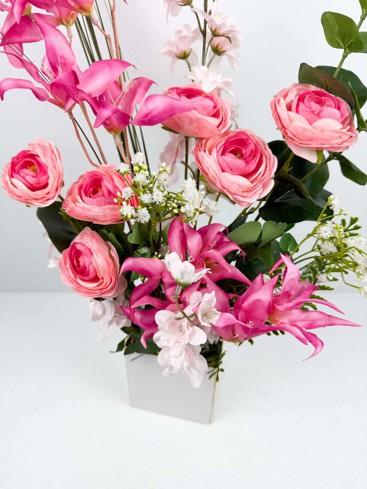Fleurs artificielles roses et blanches dans un vase carré en céramique blanc.
