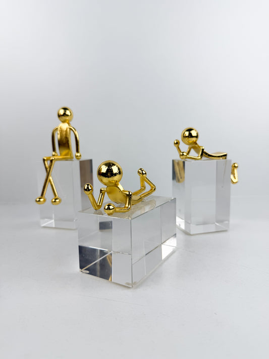 Sculptures décoratives modernes caractérisées par des personnages minimalistes dorés posés sur des bases en cristal transparent