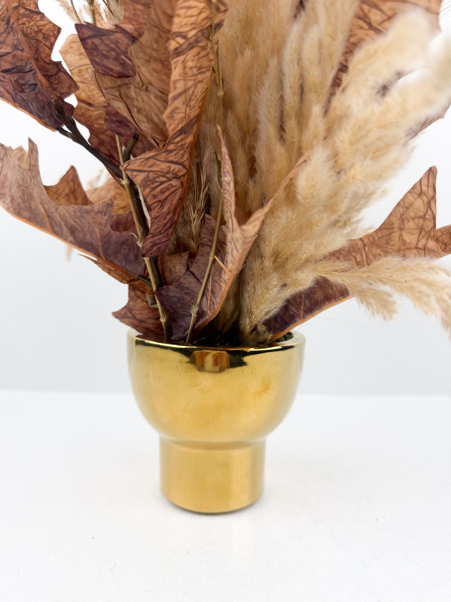 Fleurs séchées marron foncé arrangé avec élégance dans un vase en céramique doré