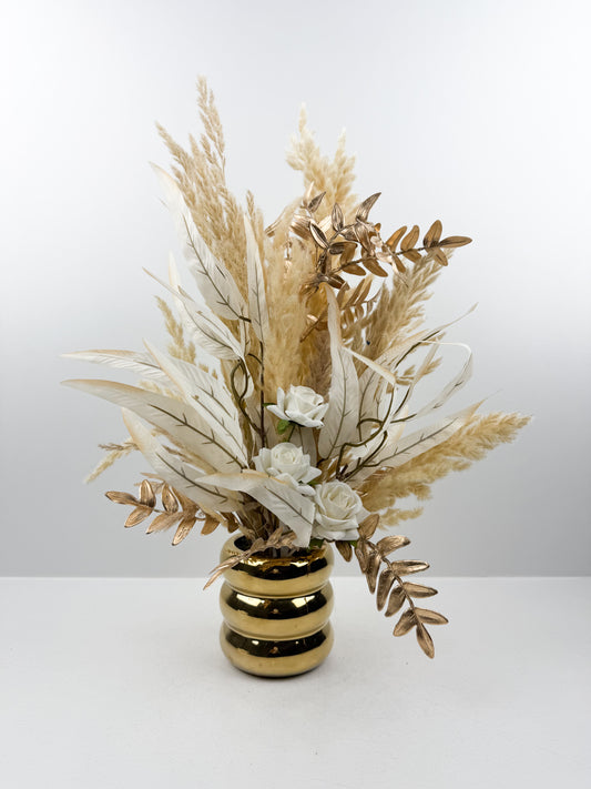 Fleurs séchées aux teintes nude délicatement arrangées dans un vase doré élégant.
