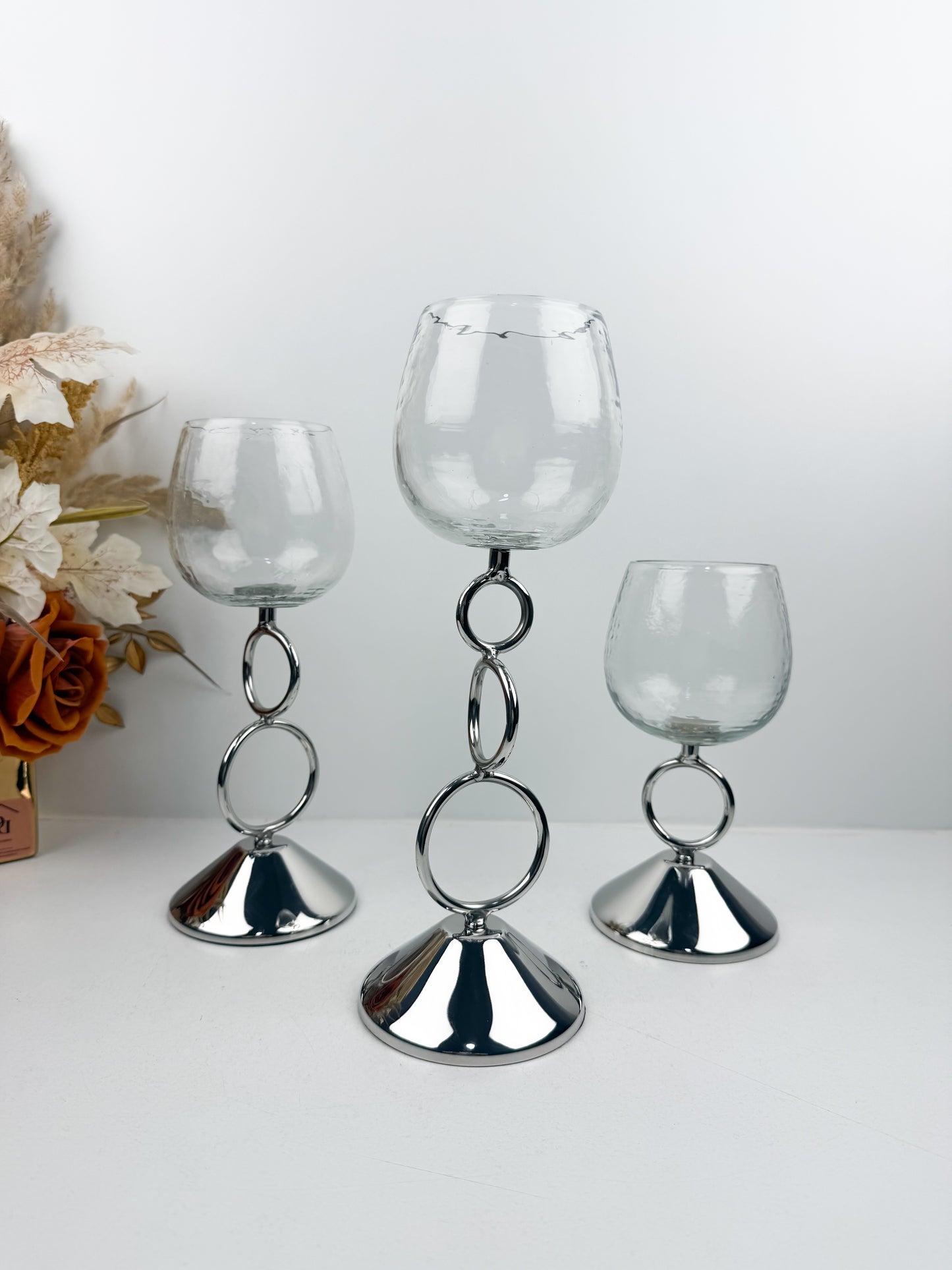 Bougeoirs décoratifs élégants avec coupe transparente et tige métallique argentée ornée d'anneaux entrelacés.