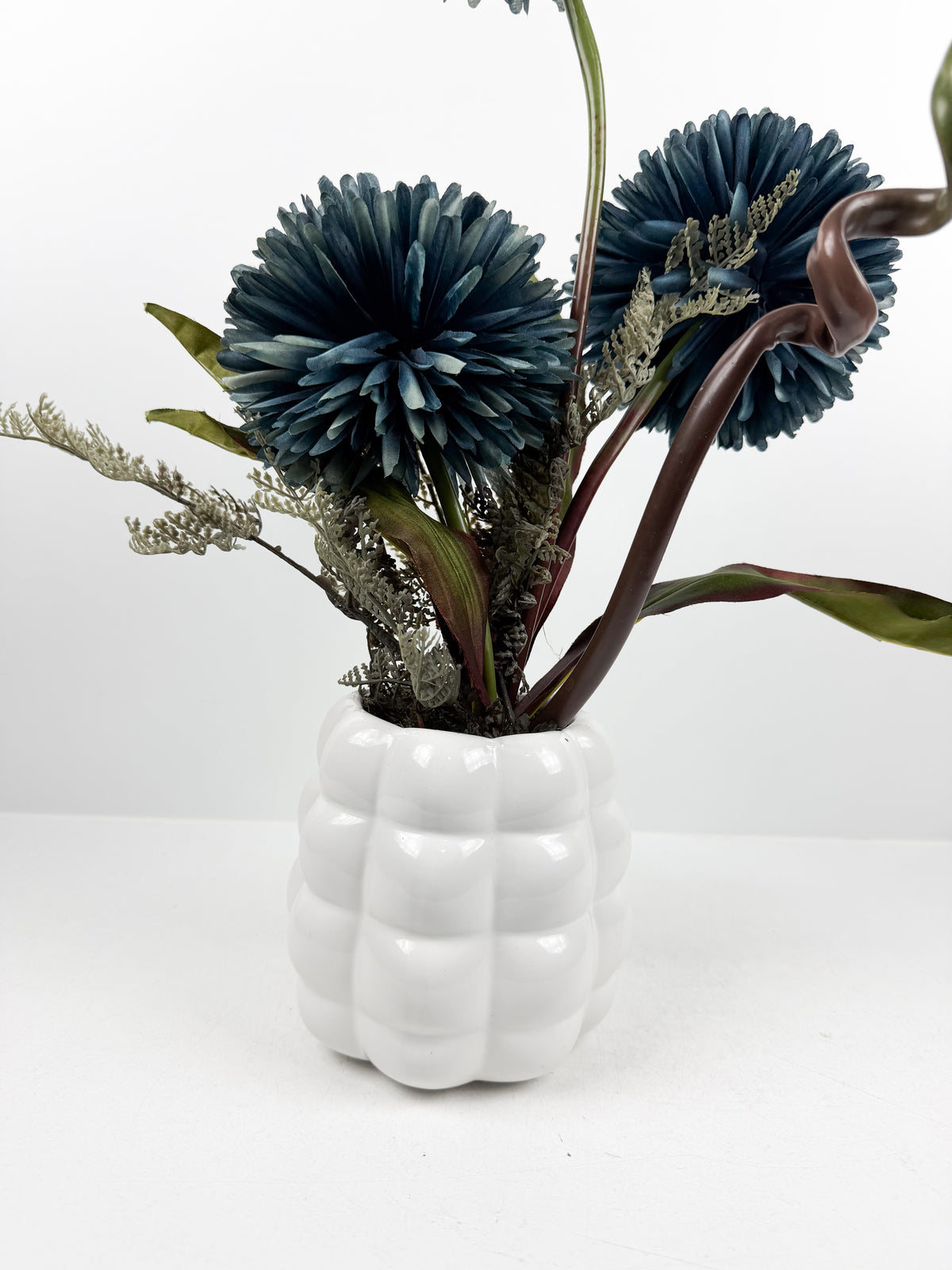 Fleurs artificielles élégantes en forme de pompons éclatantes dans un vase blanc de forme ronde.