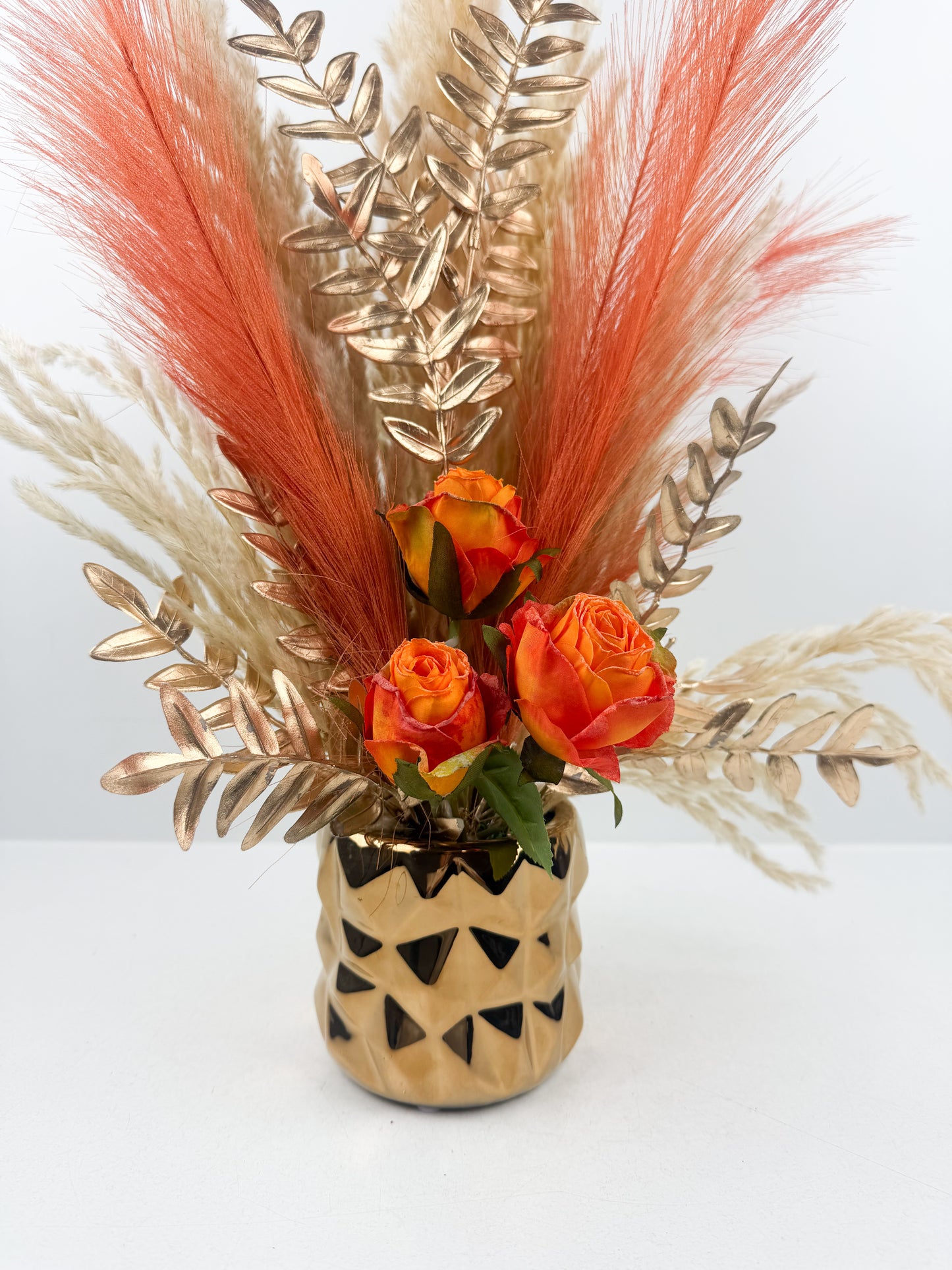 Fleurs séchées élégantes aux teintes orangées, arrangées avec raffinement dans un vase doré de luxe.