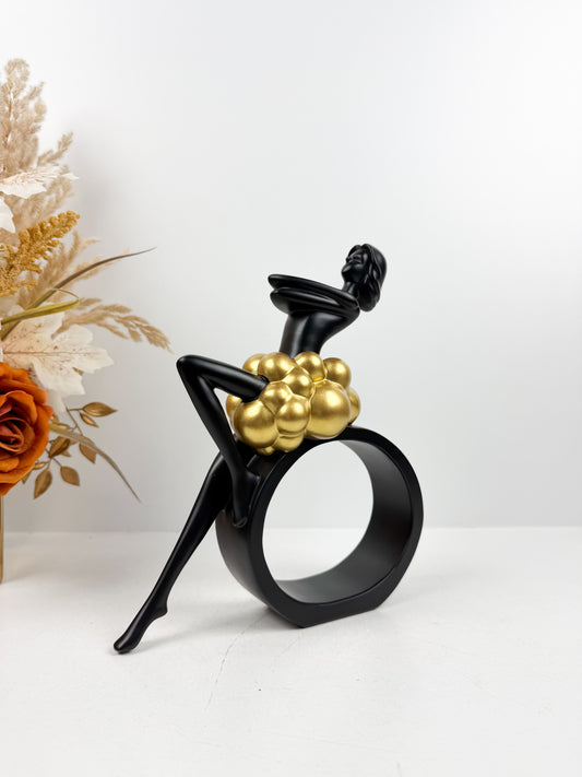 Sculpture décorative en résine noire d'une féminine assise sur un cercle avec détails de sphères dorées.
