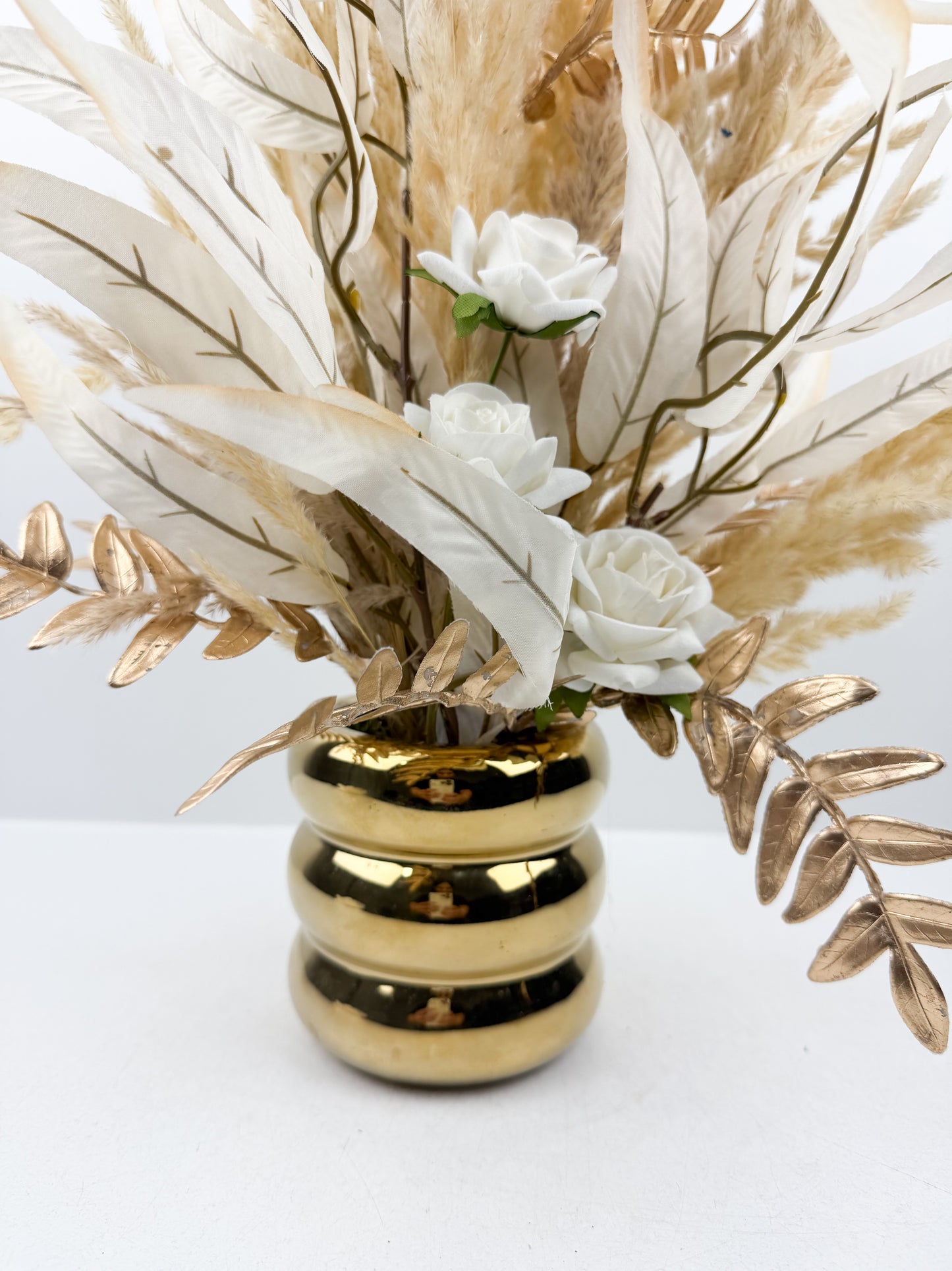 Fleurs séchées aux teintes nude délicatement arrangées dans un vase doré élégant.