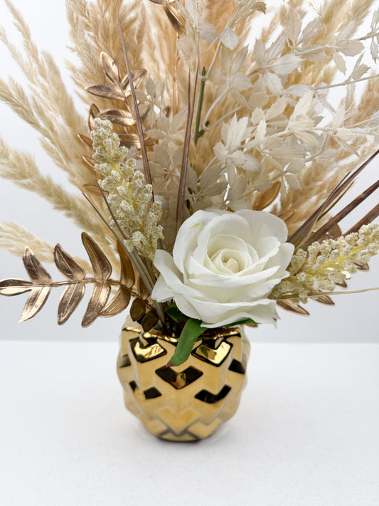 Fleurs séchées beige rehaussée d'une fleur blanche délicate présentée dans un vase en céramique doré aux lignes épurées.