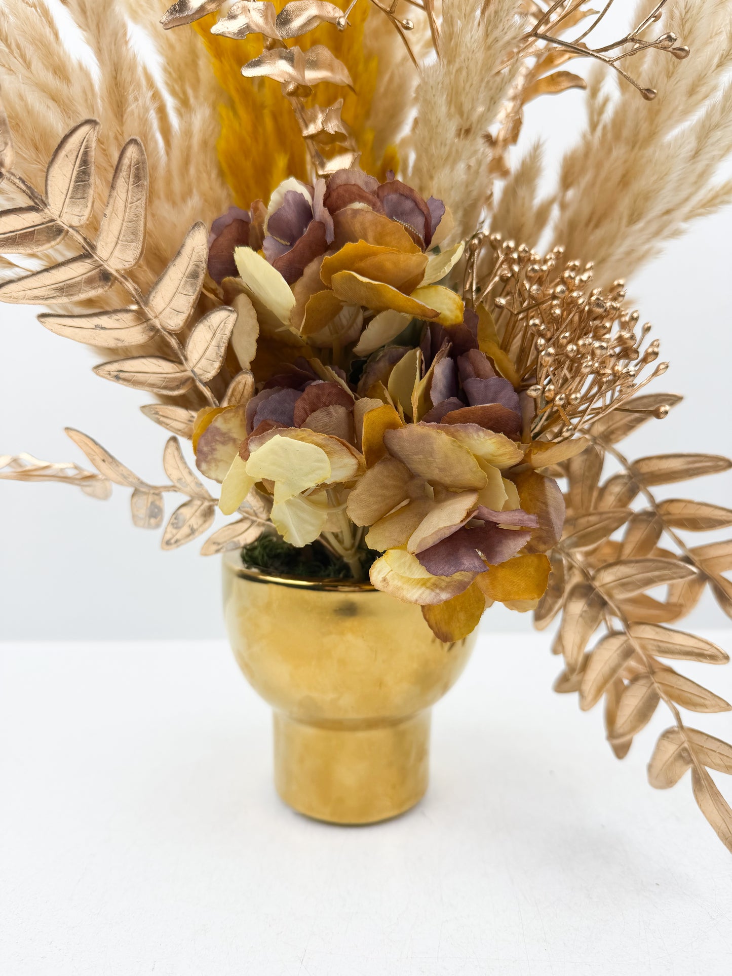 Fleurs séchées marron foncé arrangé avec élégance dans un vase en céramique doré