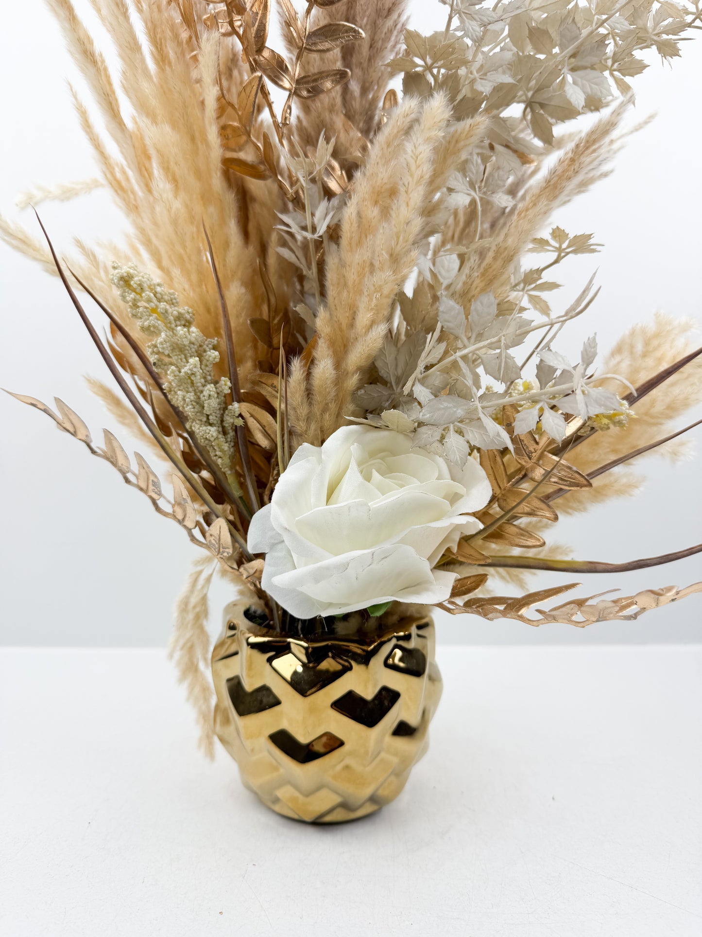 Fleurs séchées beige rehaussée d'une fleur blanche délicate dans un vase en céramique doré aux lignes épurées