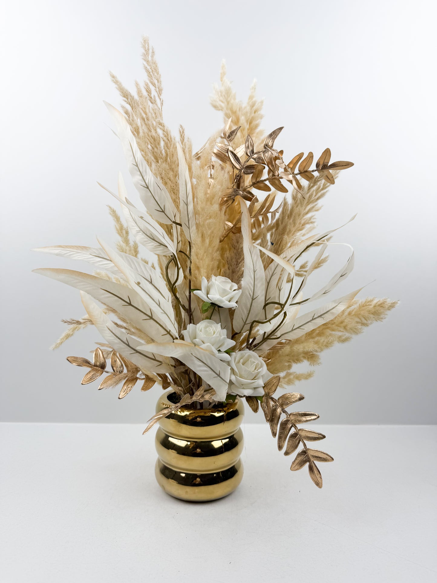 Fleurs séchées aux teintes nude délicatement arrangées dans un vase doré élégant.