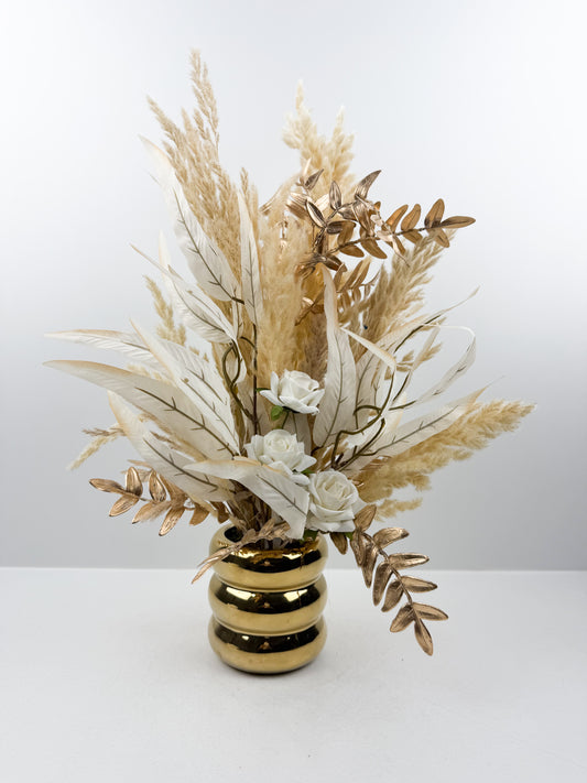 Fleurs séchées aux teintes nude délicatement arrangées dans un vase doré élégant.