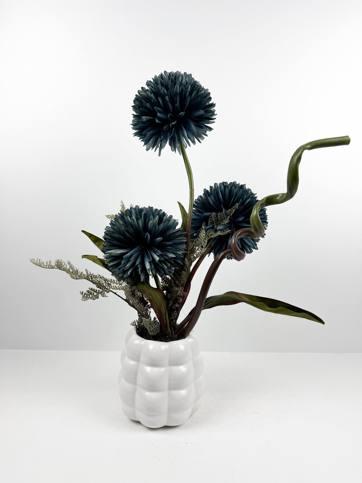 Fleurs artificielles élégantes en forme de pompons éclatantes dans un vase blanc de forme ronde.