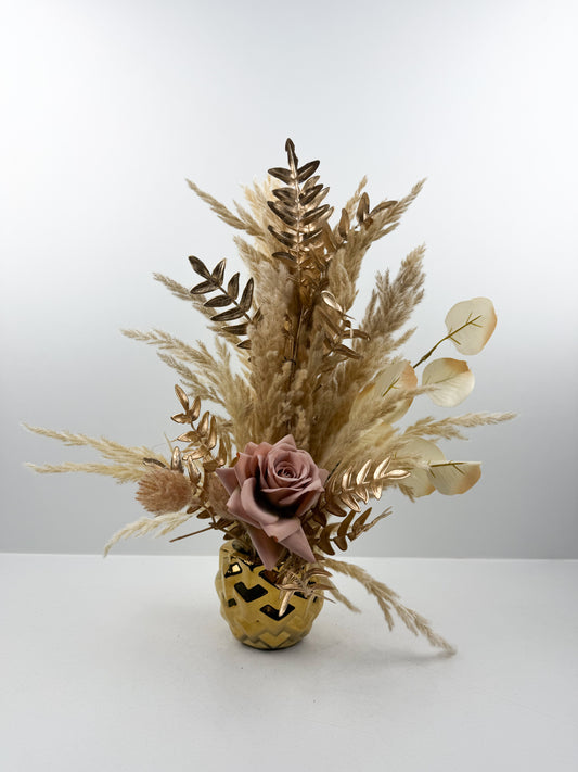 Fleurs séchées rehaussée d'une fleur rose dans un vase en céramique doré aux lignes épurées.