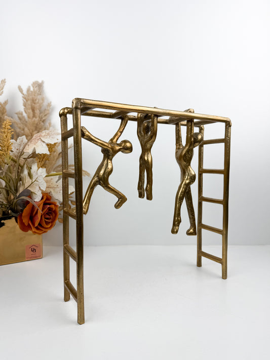 Sculpture décorative en métal mettant en scène trois personnages suspendus à une structure d'échelle.