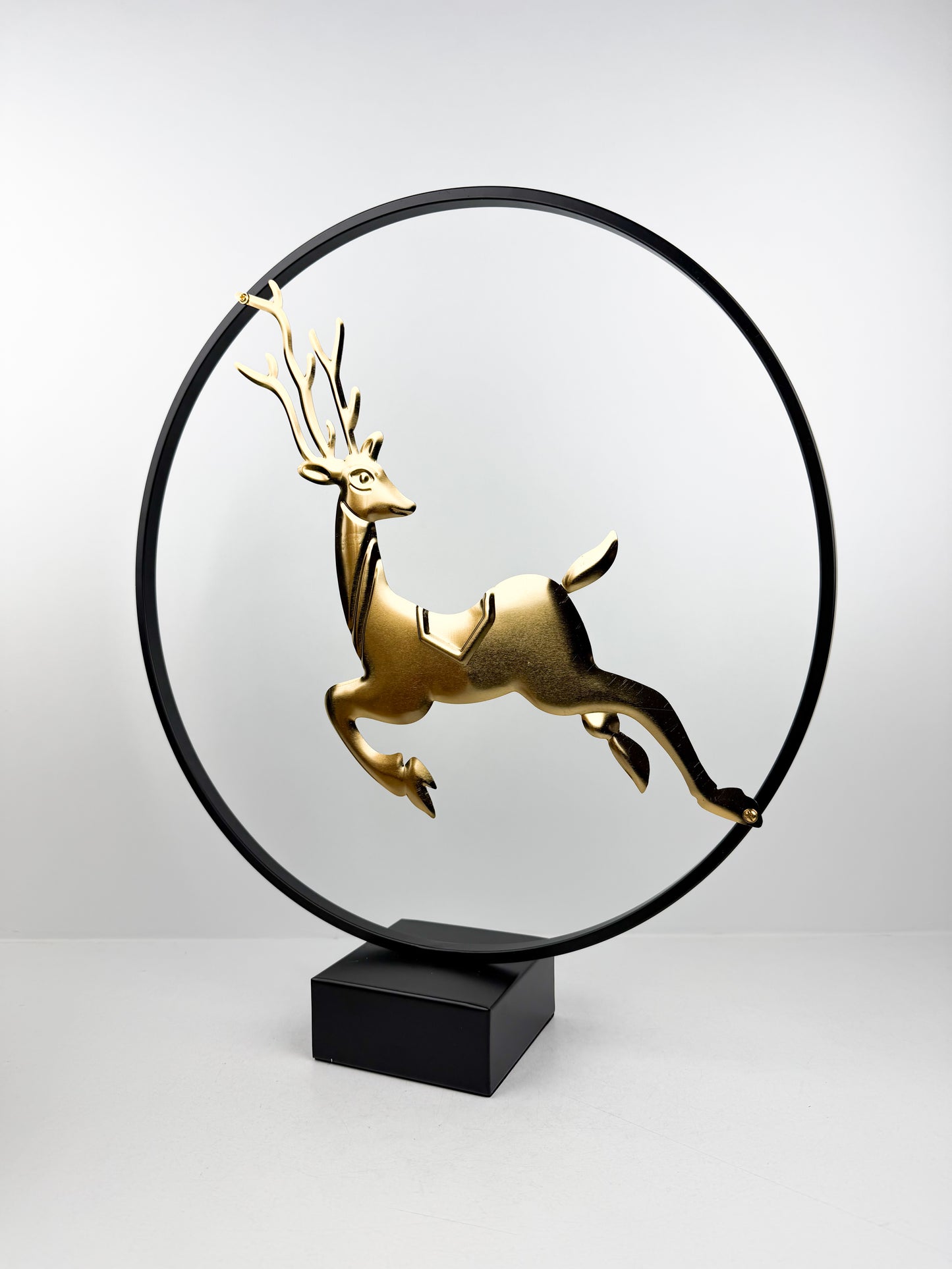Sculpture décorative moderne représentant un cerf doré bondissant, encadré dans un cercle métallique noir épuré.