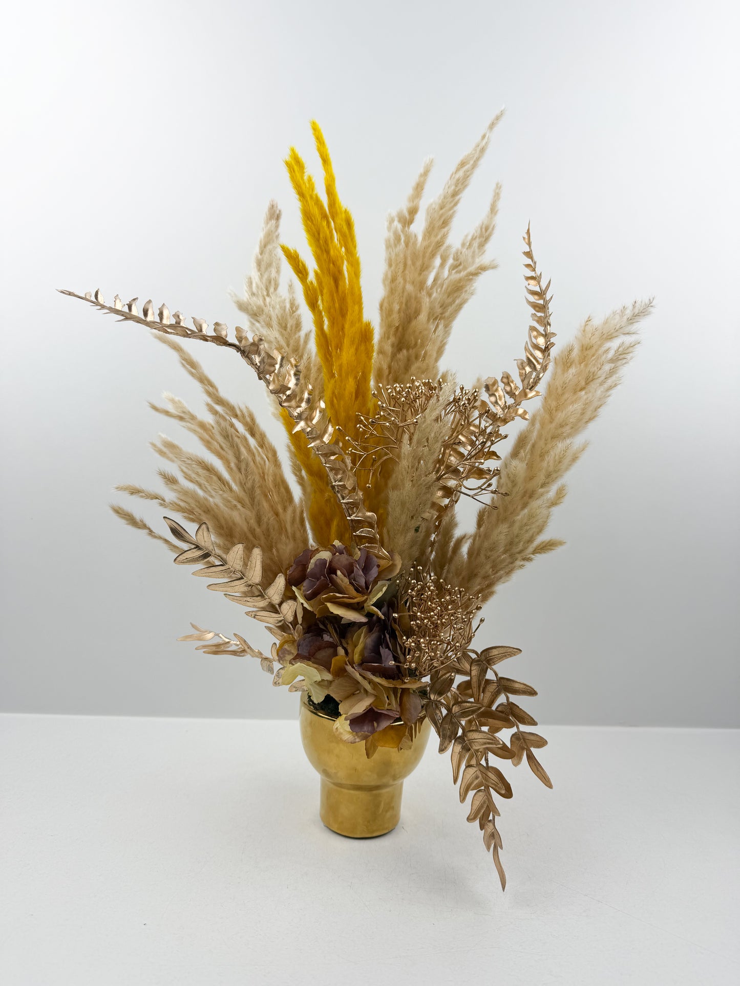 Fleurs séchées marron foncé arrangé avec élégance dans un vase en céramique doré