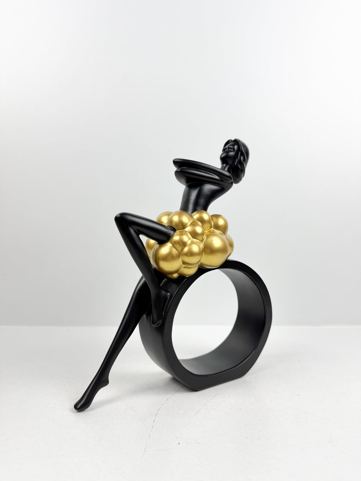 Sculpture décorative en résine noire d'une féminine assise sur un cercle avec détails de sphères dorées.