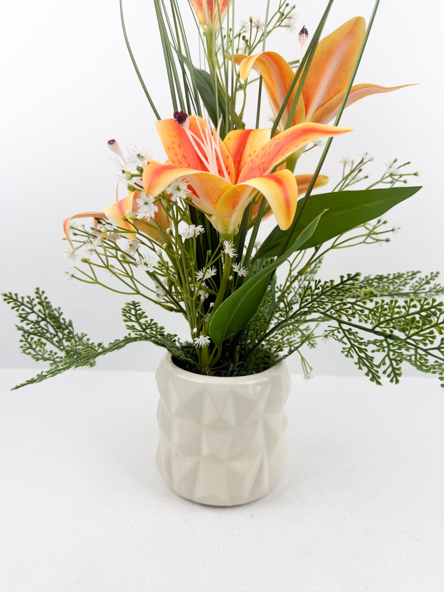 Fleurs artificielles orange  délicates présentées dans un élégant pot blanc en céramique de luxe