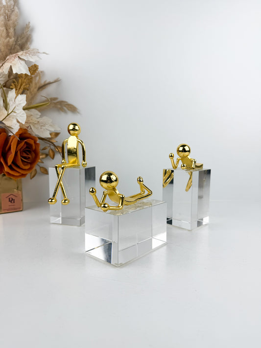 Sculptures décoratives modernes caractérisées par des personnages minimalistes dorés posés sur des bases en cristal transparent