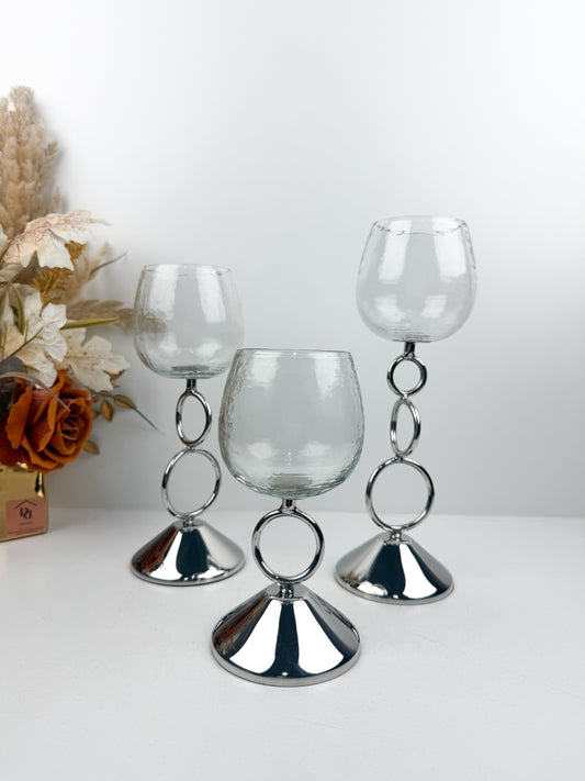 Bougeoirs décoratifs élégants avec coupe transparente et tige métallique argentée ornée d'anneaux entrelacés.