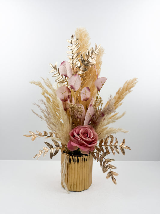 Fleurs séchées marron rehaussée d'une fleur rose délicate dans un vase en céramique doré au design élégant et luxueux.