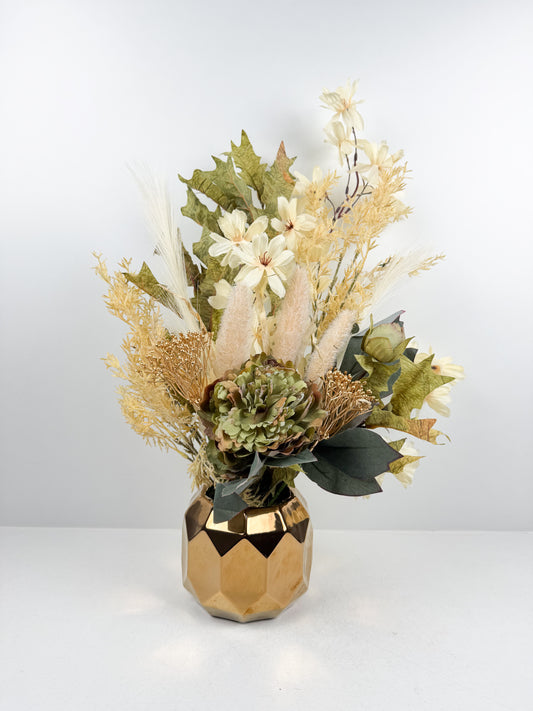 Arrangement de fleurs séchées vert doux dans un vase géométrique doré facetté.