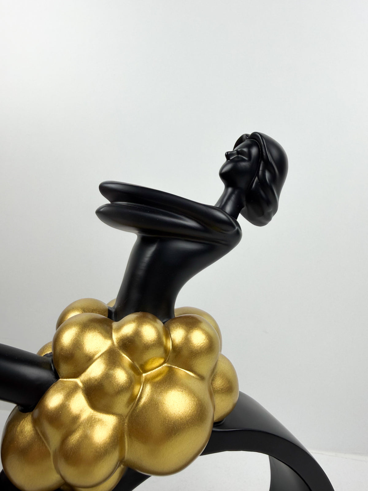 Sculpture décorative en résine noire d'une féminine assise sur un cercle avec détails de sphères dorées.