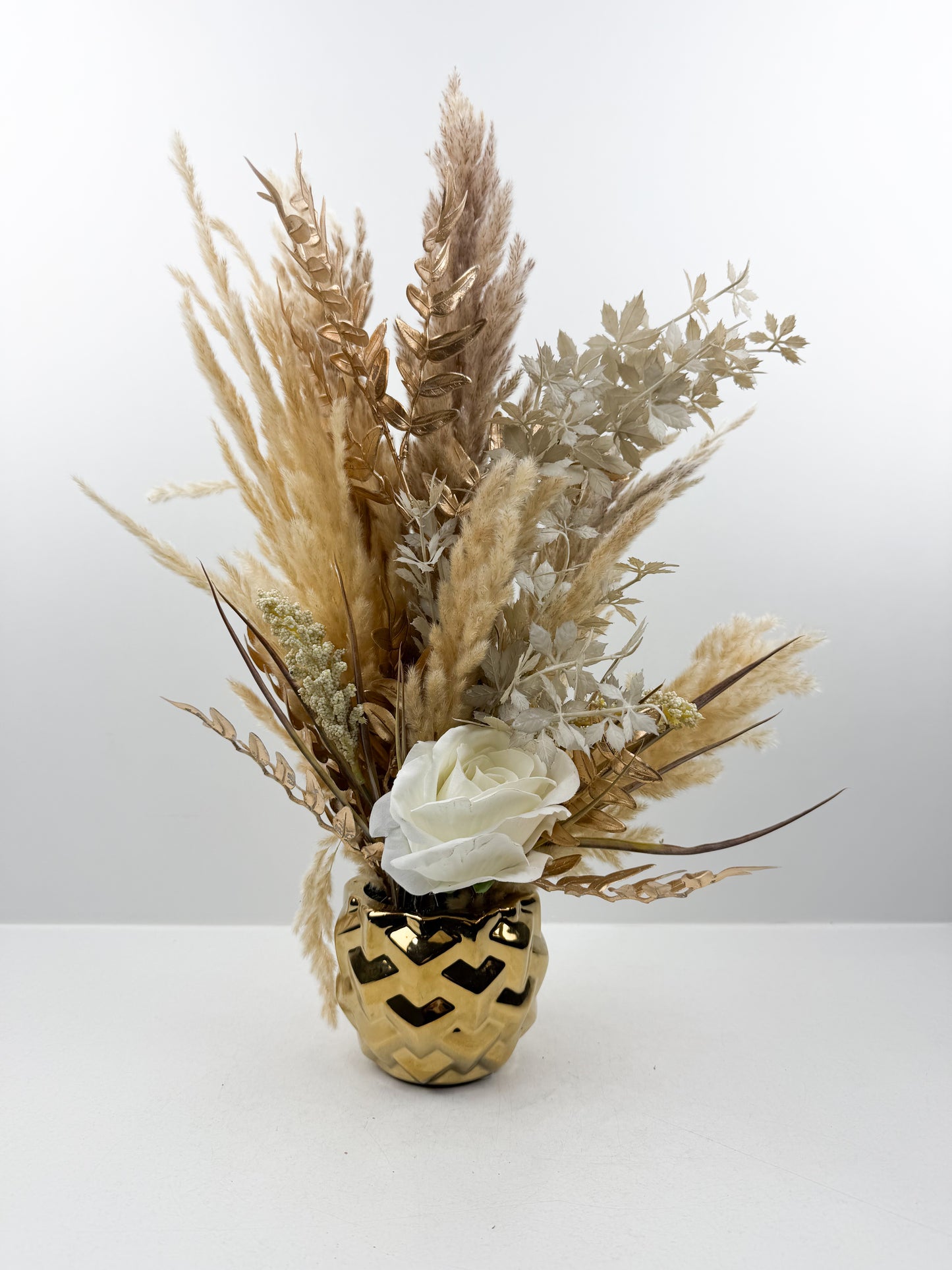Fleurs séchées beige rehaussée d'une fleur blanche délicate dans un vase en céramique doré aux lignes épurées
