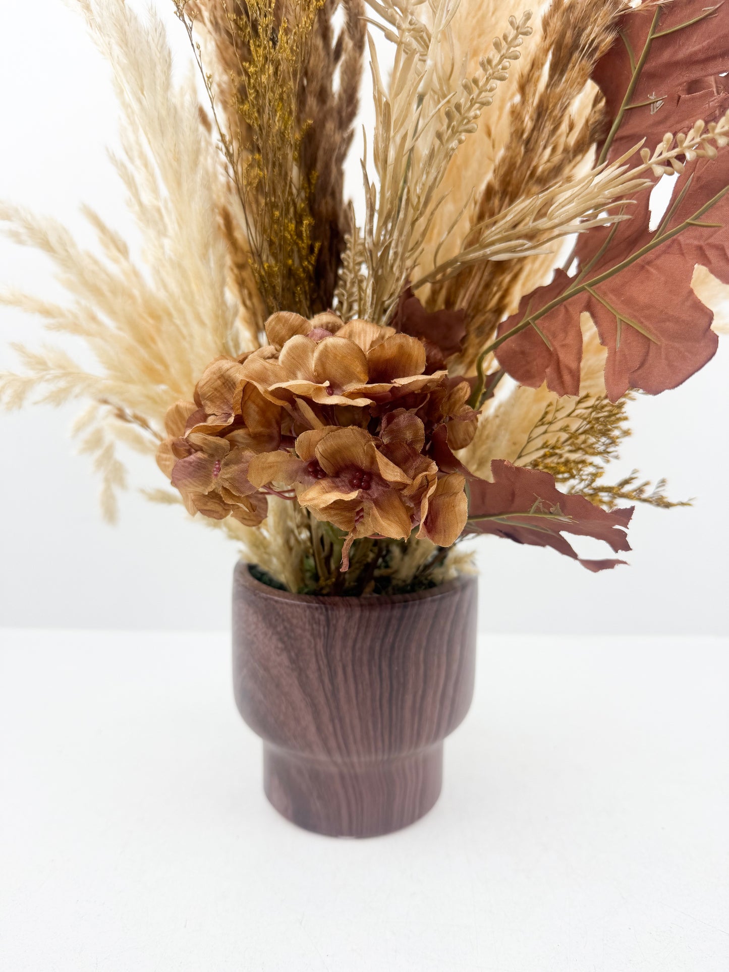 Fleurs séchées aux teintes chaudes et naturelles, présenté dans un élégant vase en bois marron