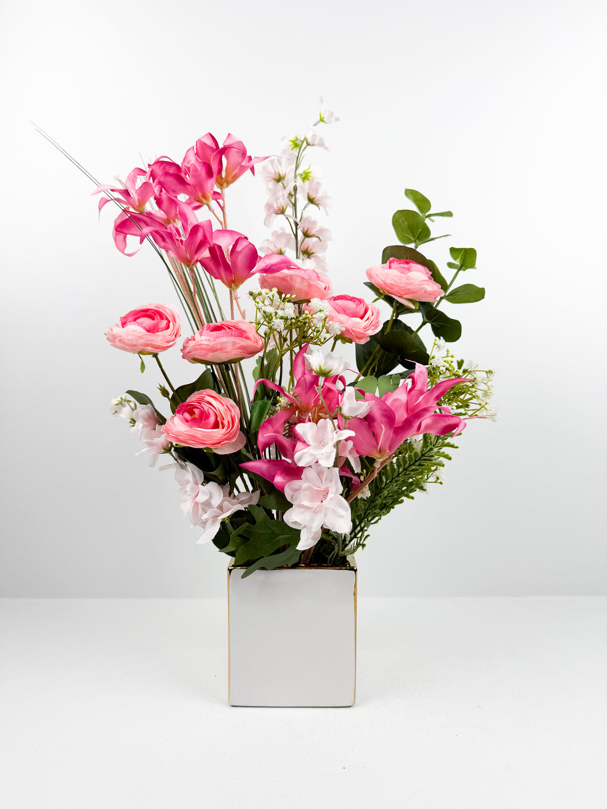 Fleurs artificielles roses et blanches dans un vase carré en céramique blanc.