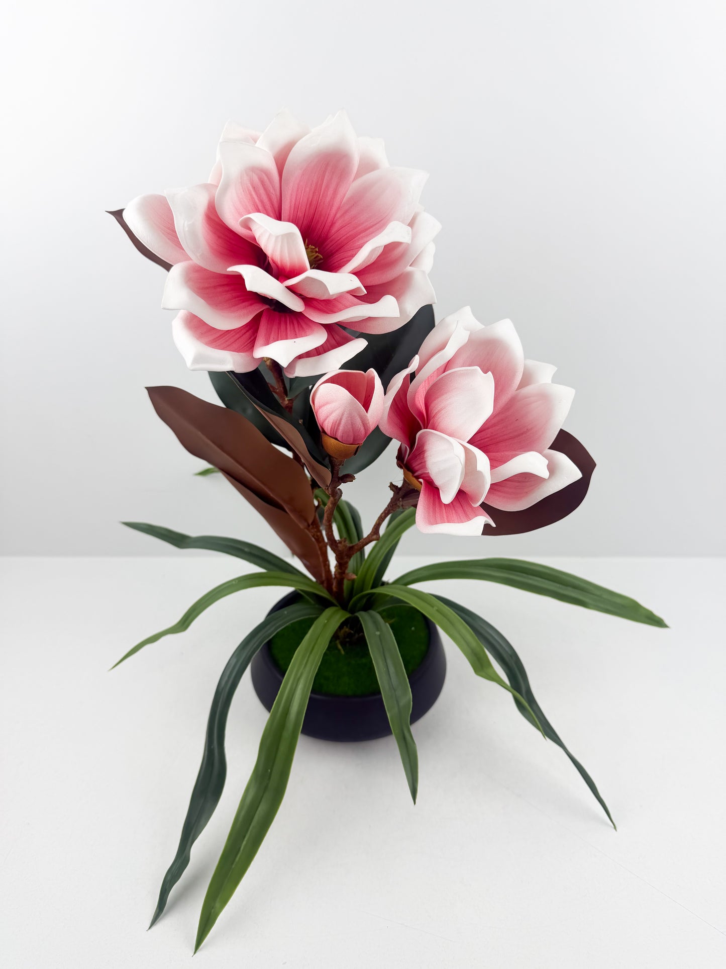 Fleurs artificielles roses haut de gamme associées à un élégant pot en céramique noir.