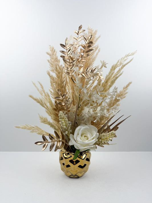 Fleurs séchées beige rehaussée d'une fleur blanche délicate présentée dans un vase en céramique doré aux lignes épurées.