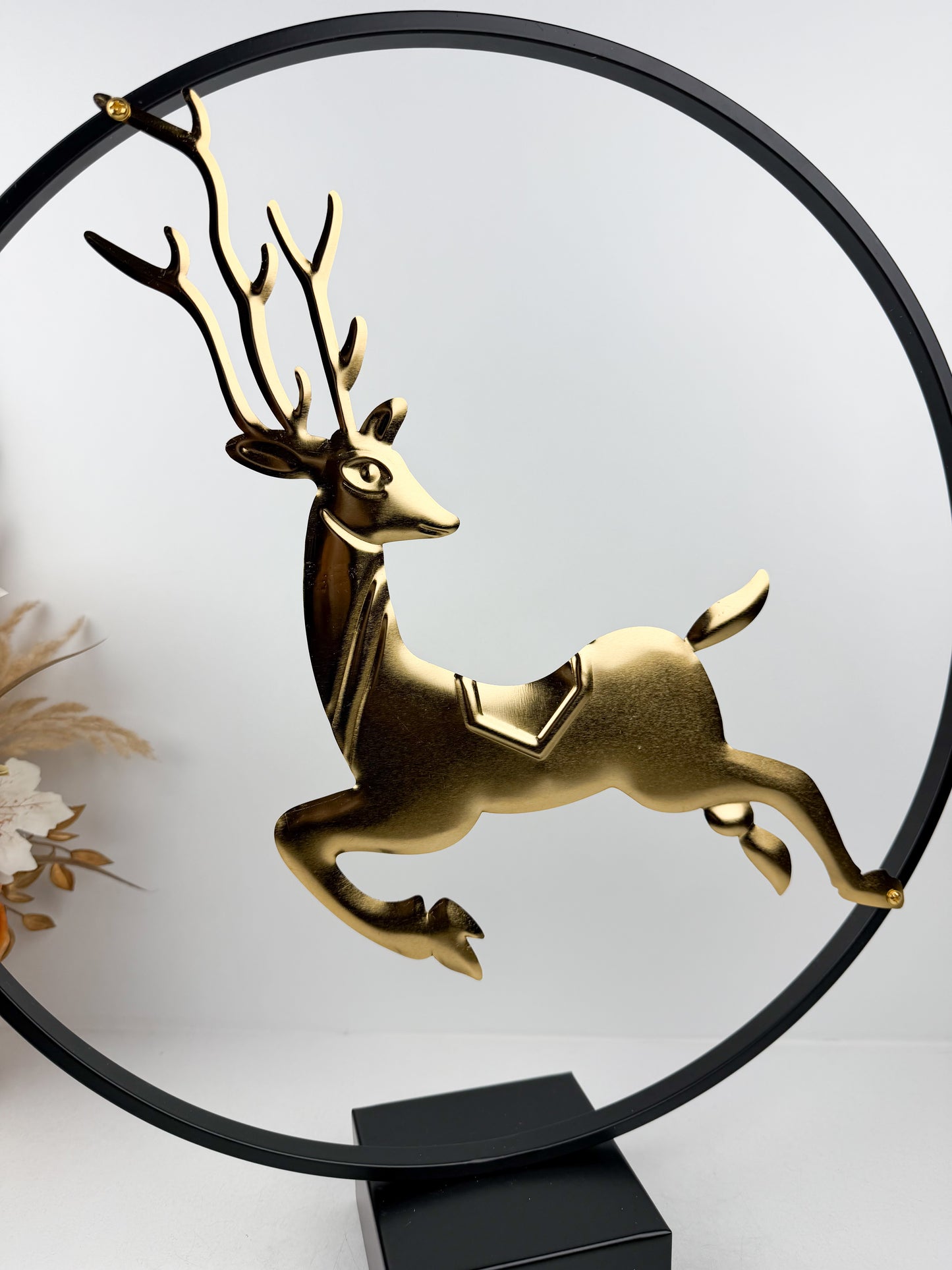 Sculpture décorative moderne représentant un cerf doré bondissant, encadré dans un cercle métallique noir épuré.