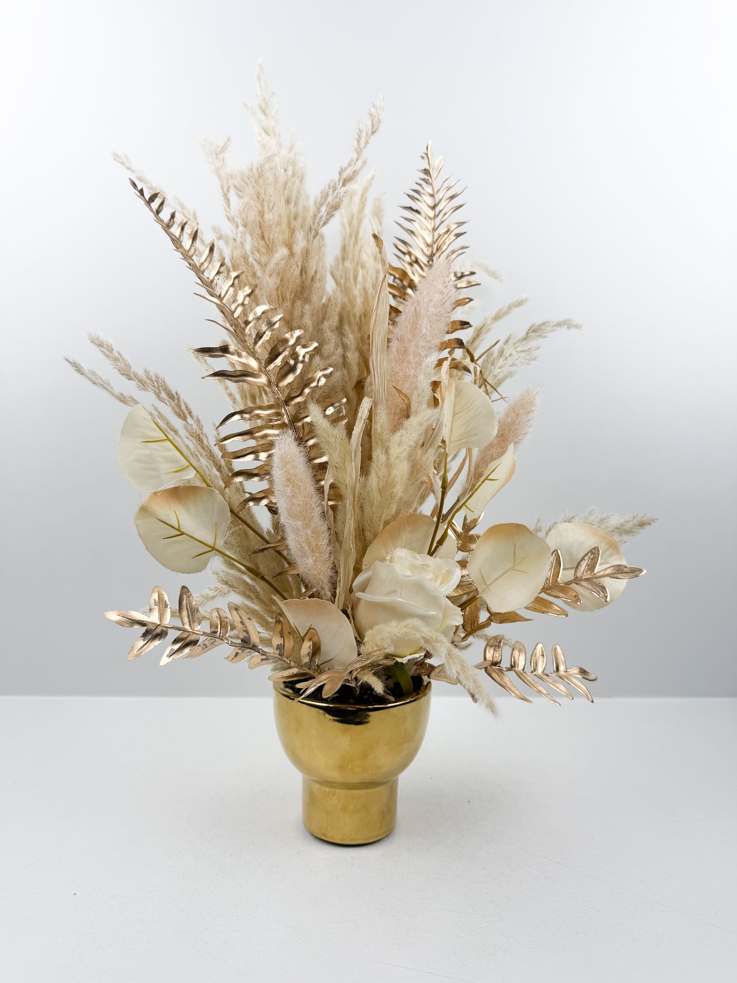 Fleurs séchées beige arrangé avec élégance dans un vase en céramique doré