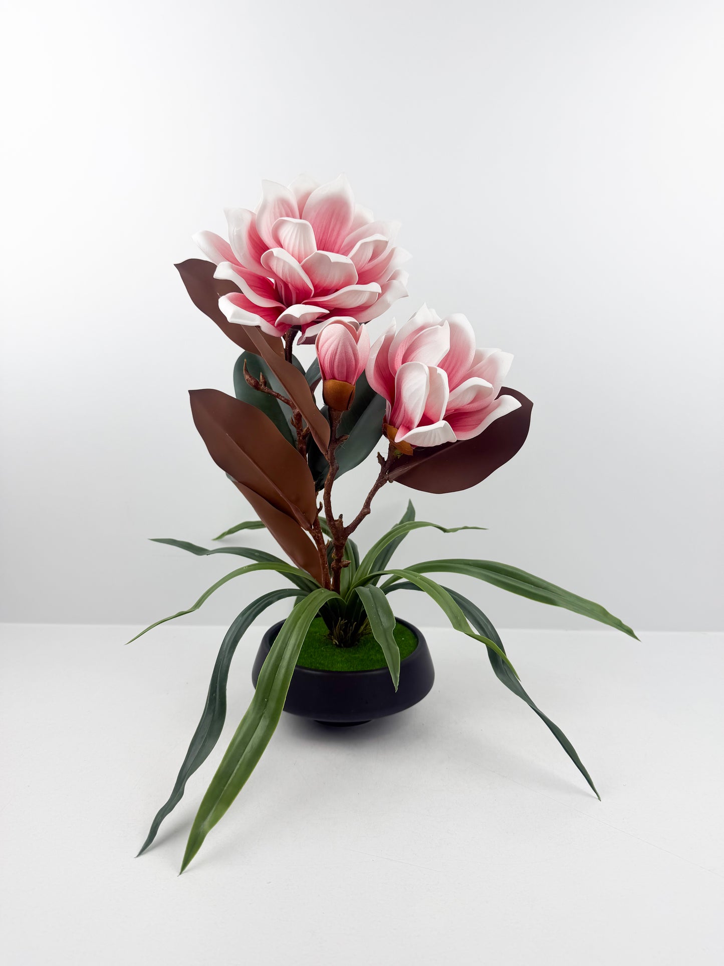 Fleurs artificielles roses haut de gamme associées à un élégant pot en céramique noir.