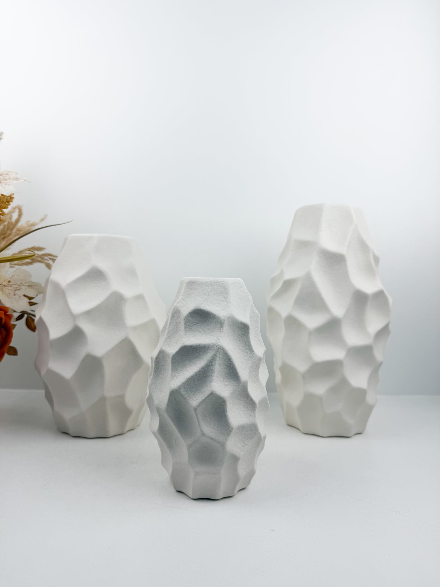 Trio de vases blanches aux formes sculpturales épurées.