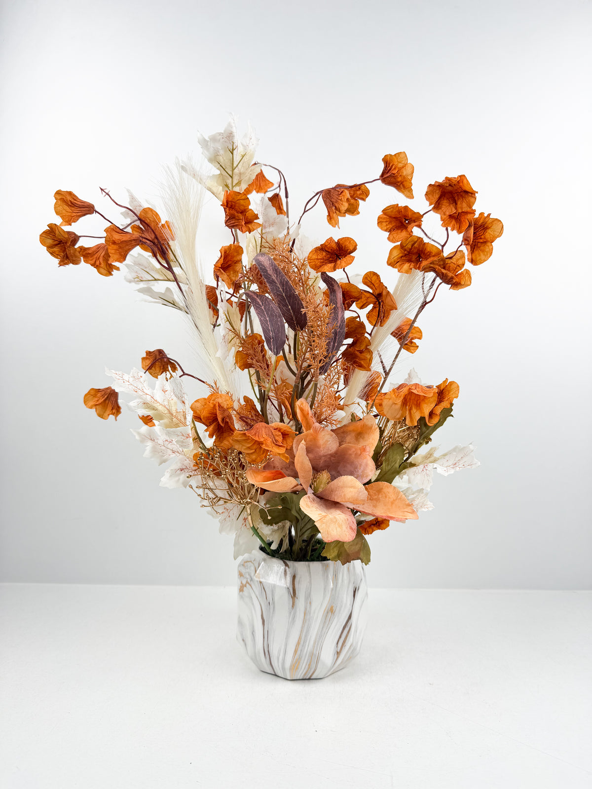 Magnifique fleurs aux nuances chaleureuses d'orange cuivré dans un élégant vase en céramique à effet marbré.