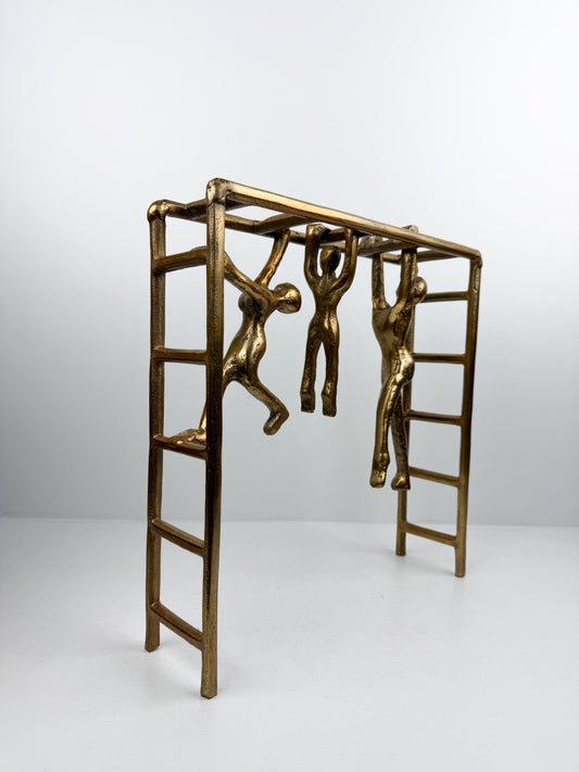 Sculpture décorative en métal mettant en scène trois personnages suspendus à une structure d'échelle.