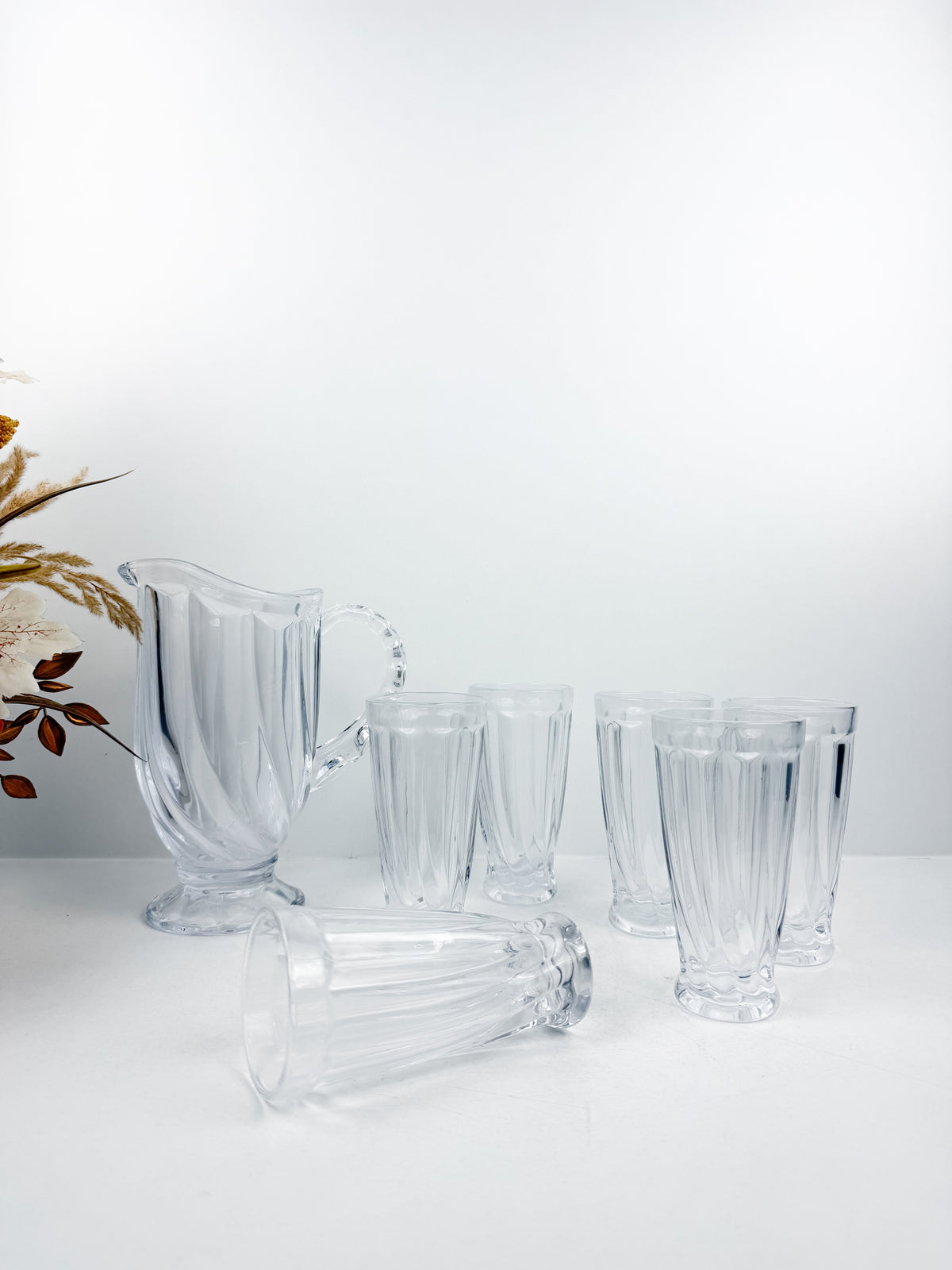 Service en verre transparent composé d'une carafe et de six verres assortis à motifs géométriques.