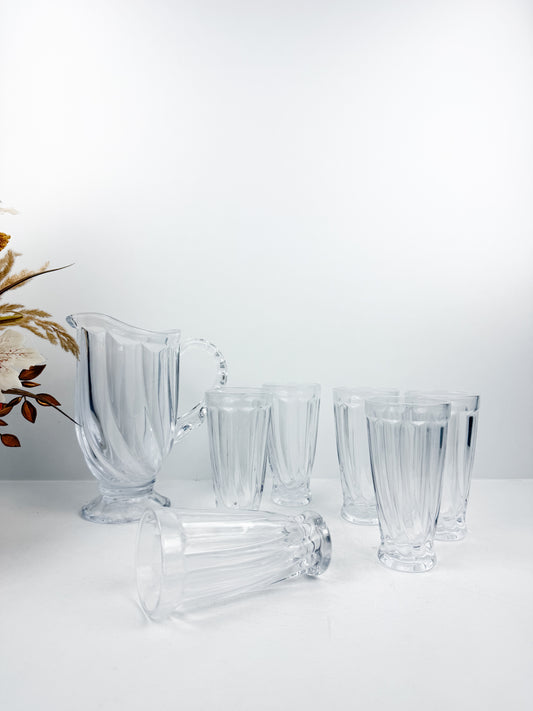 Service en verre transparent composé d'une carafe et de six verres assortis à motifs géométriques.