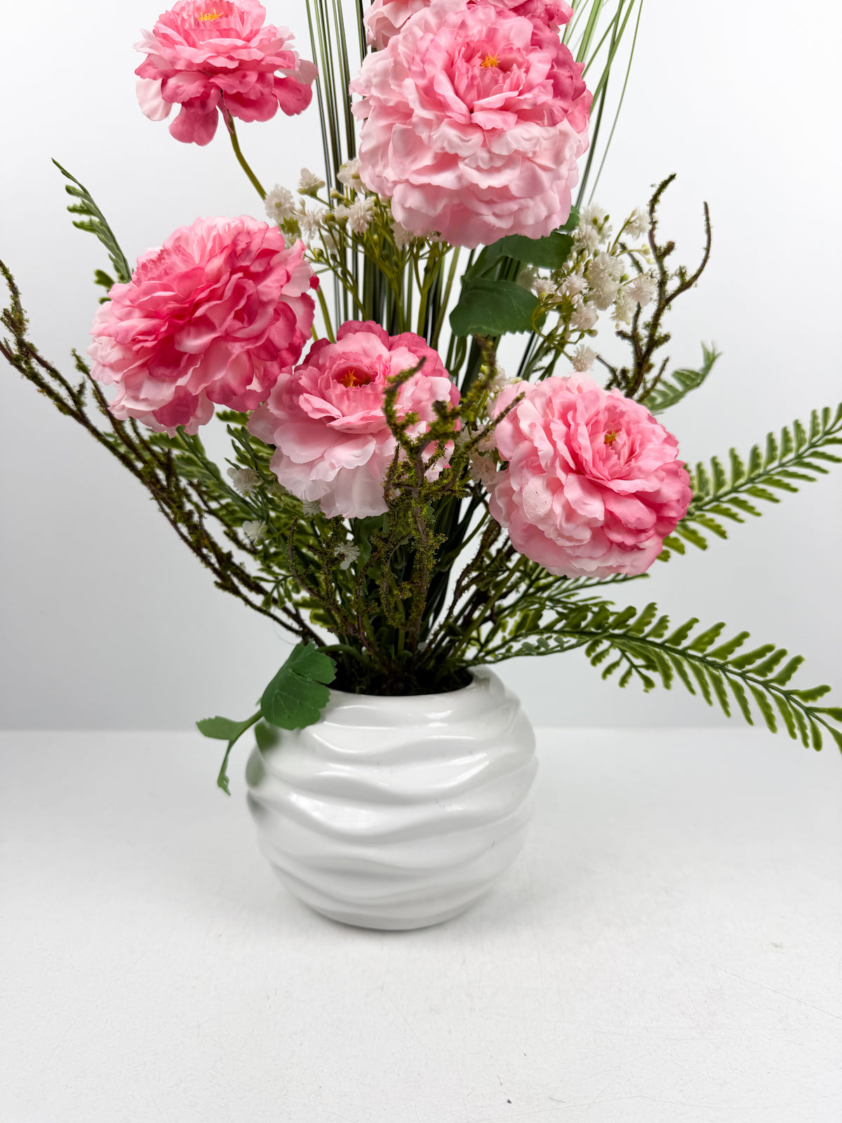 Fleurs roses raffinées présenté dans un magnifique vase en céramique blanche texturée.