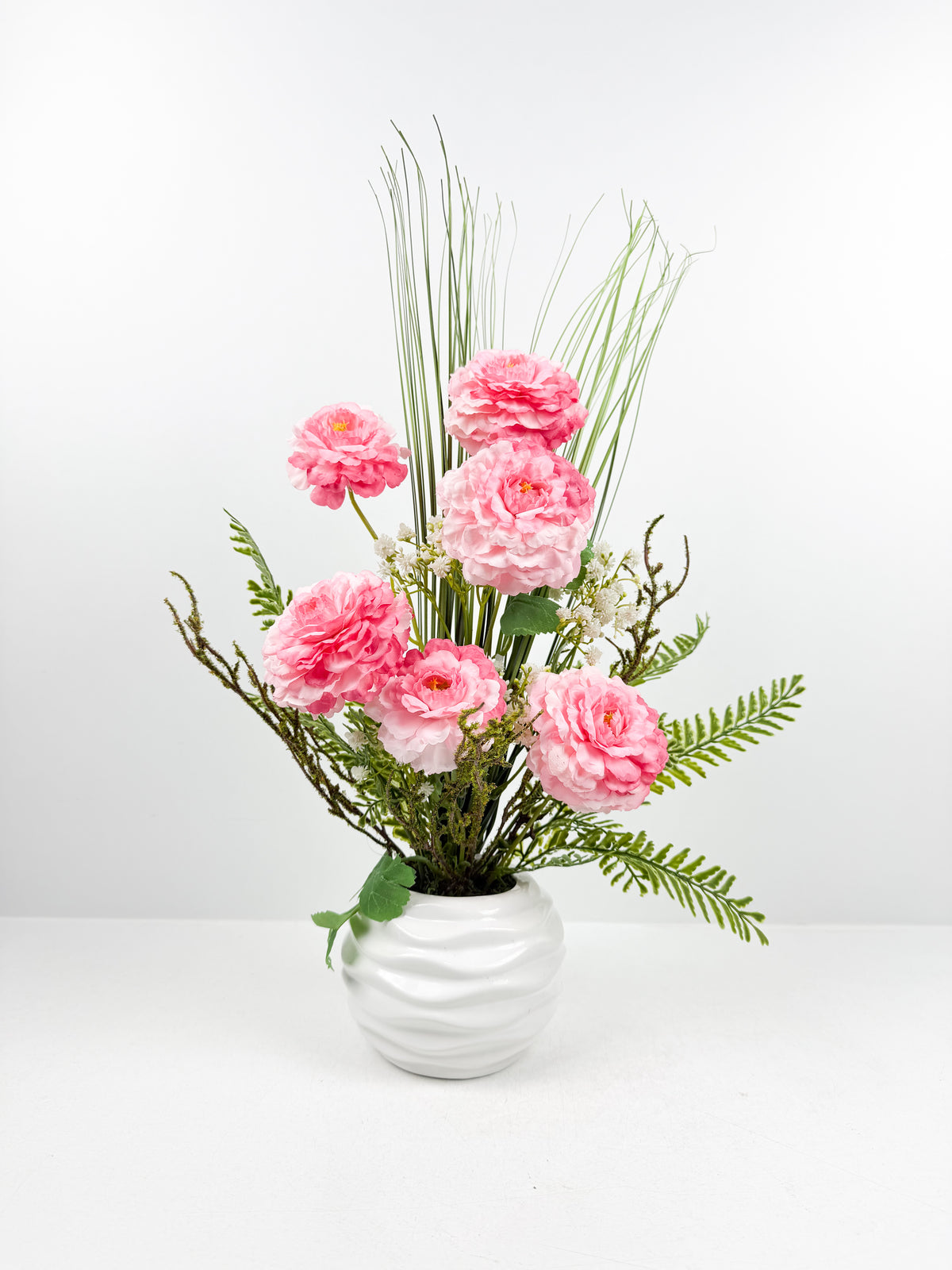 Fleurs roses raffinées présenté dans un magnifique vase en céramique blanche texturée.