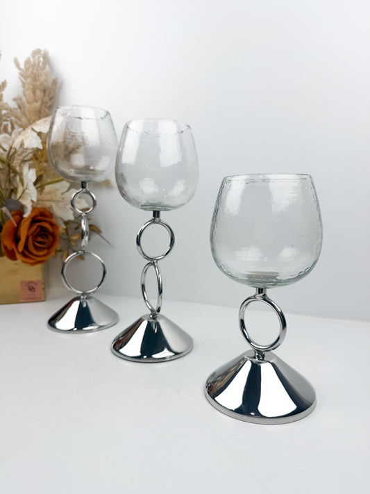 Bougeoirs décoratifs élégants avec coupe transparente et tige métallique argentée ornée d'anneaux entrelacés.