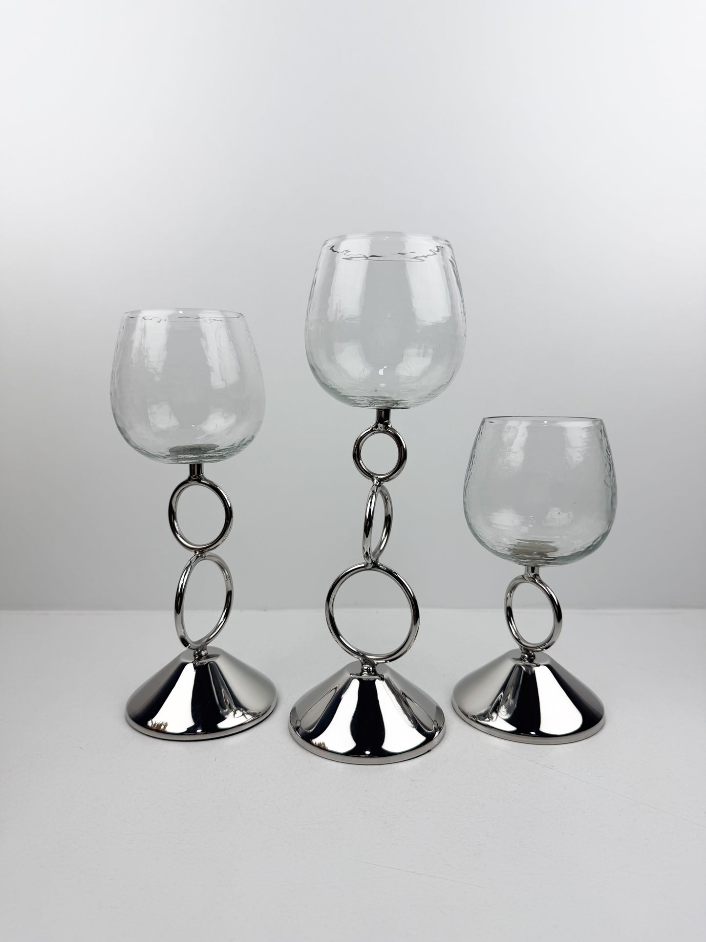 Bougeoirs décoratifs élégants avec coupe transparente et tige métallique argentée ornée d'anneaux entrelacés.