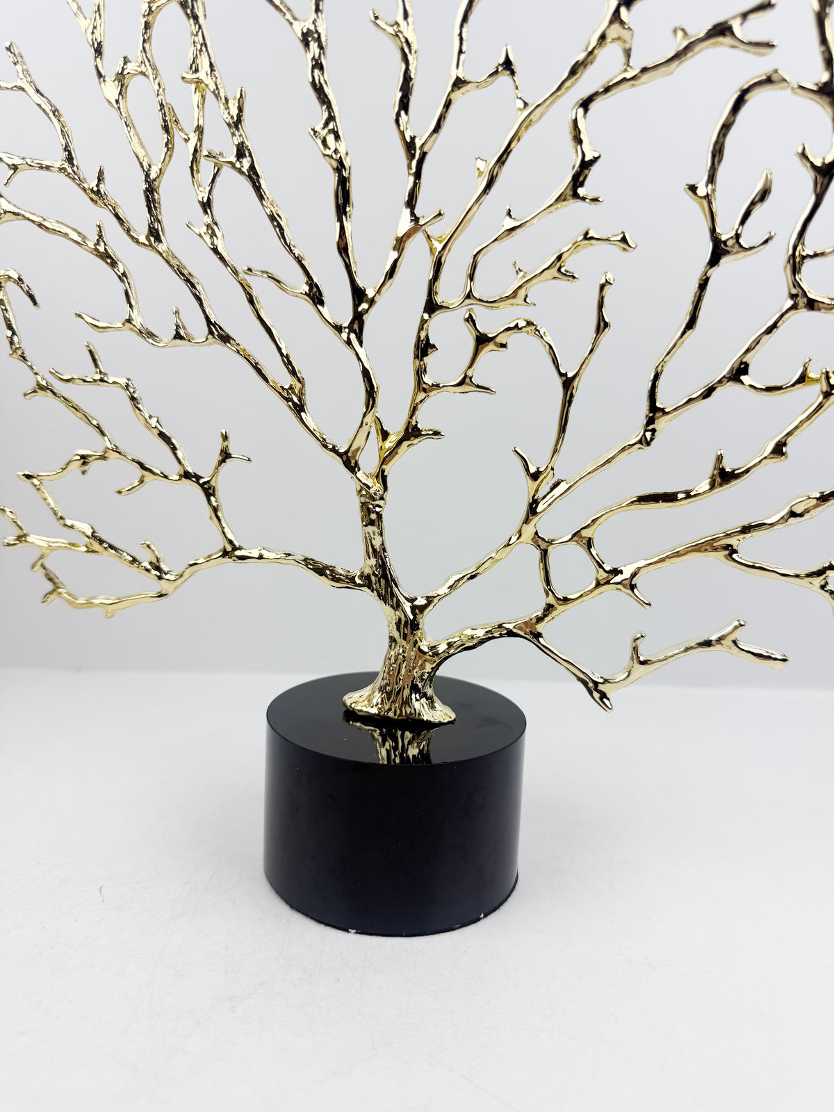 Arbre décoratif sculptural doré sur un socle en cristal noir.