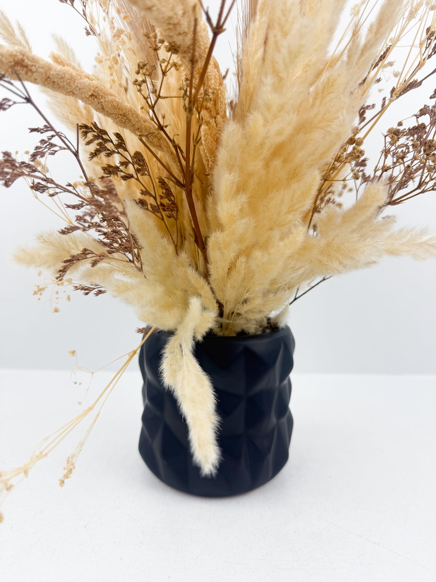 Fleurs séchées marron clair arrangées avec élégance dans une vase en céramique noir sophistiquée.