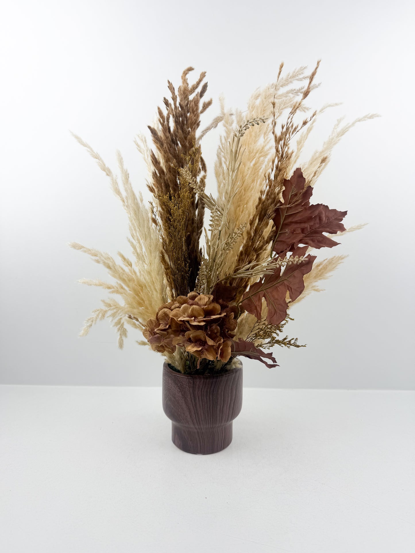 Fleurs séchées aux teintes chaudes et naturelles, présenté dans un élégant vase en bois marron
